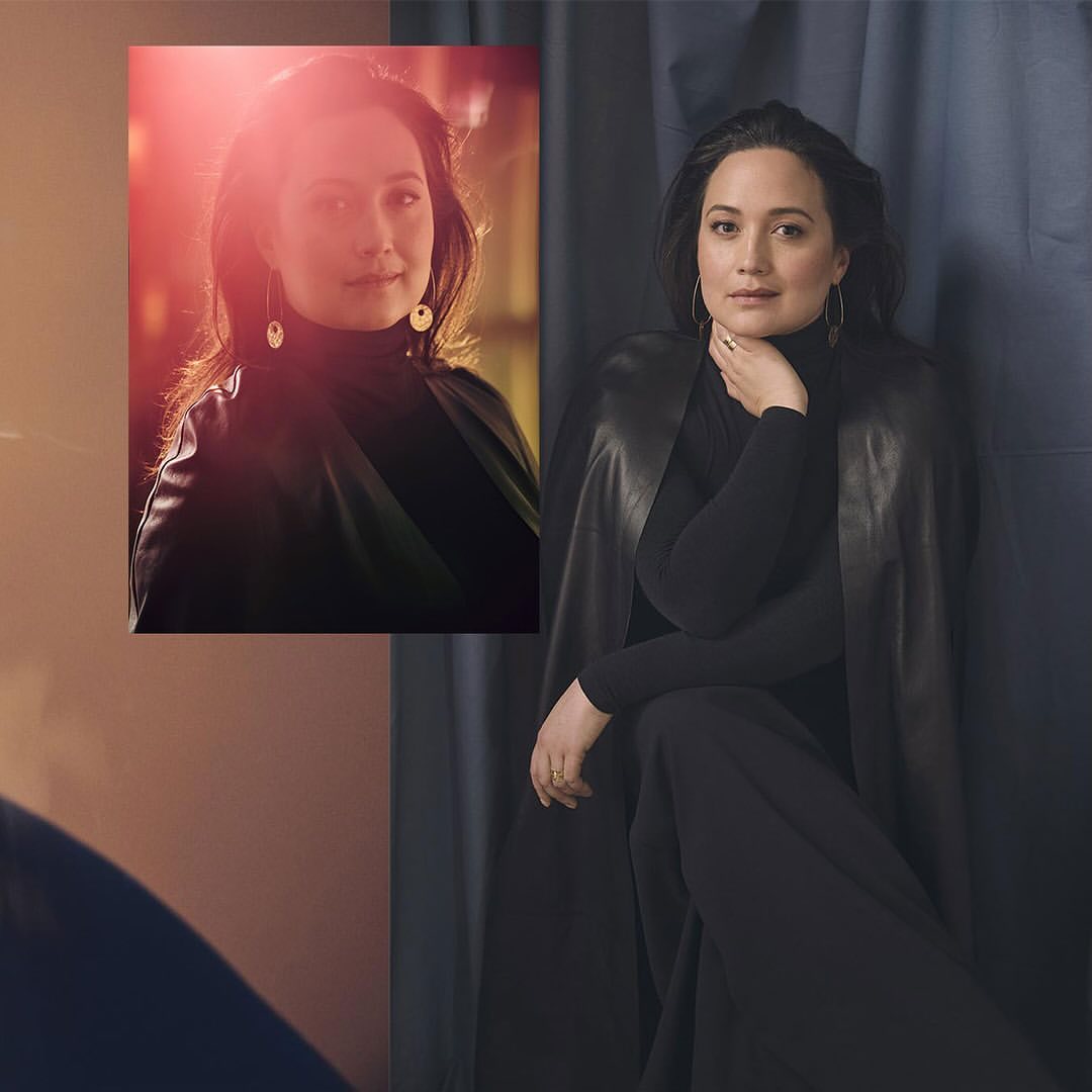 Portrait of a stylish adult woman in black leaning against a blue draped backdrop, alongside a smaller headshot of the same woman.