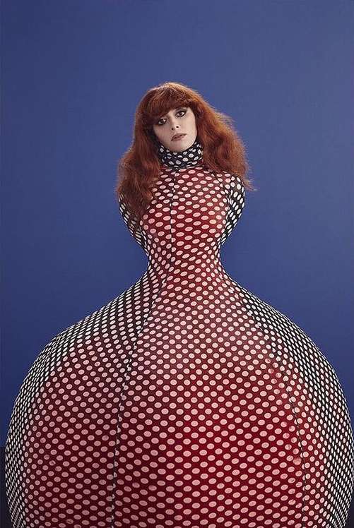 Adult woman in a red polka dot dress posing against a blue backdrop, creating a bold, eye-catching visual for fashion editorial.