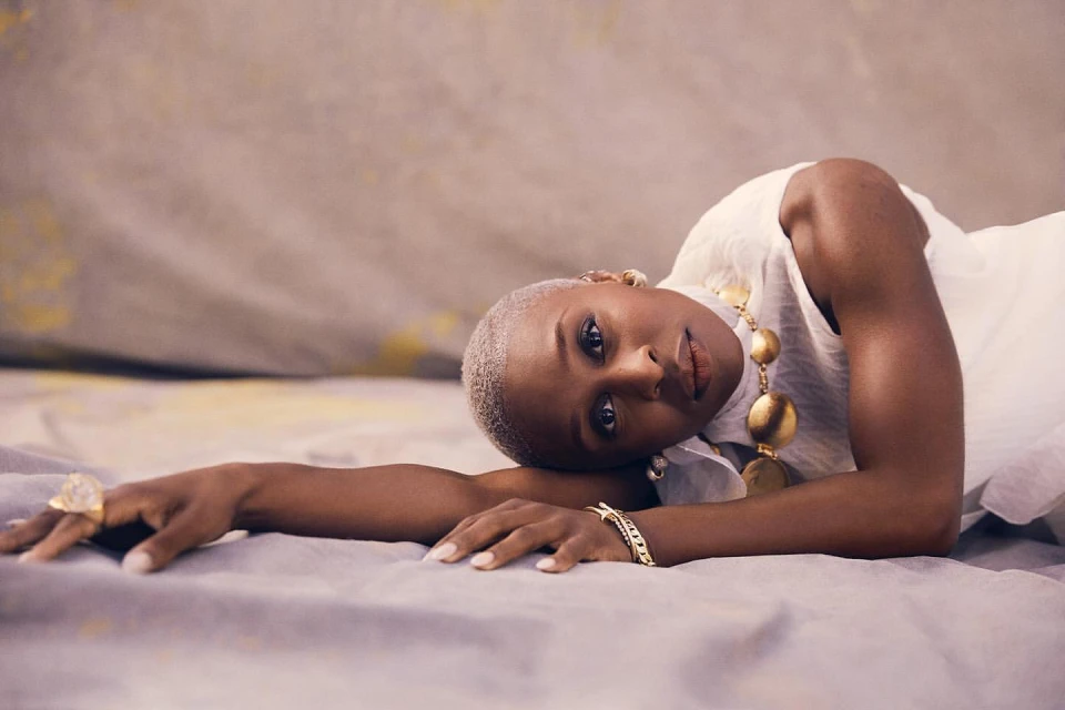 Elegant portrait of a stylish Black woman with short gray hair and jewelry, lying on gray fabric in a studio setting.