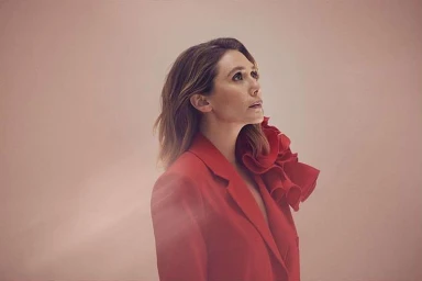 Elizabeth Olsen wearing a structured red blazer with ruffled lapel detail against a neutral backdrop