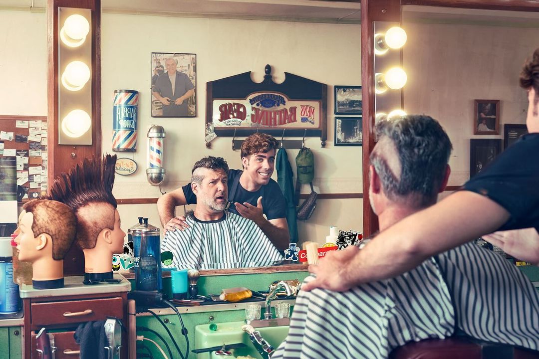 Barbershop scene features a barber cutting a customer's hair, reflected in a mirror displaying vintage decor and colorful barber poles.