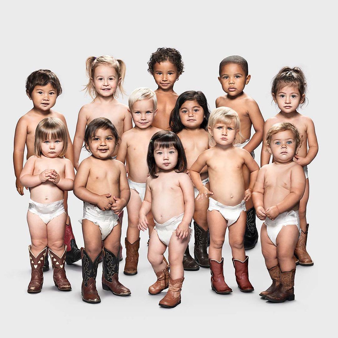 Group of toddlers wearing diapers and cowboy boots posing against a light grey backdrop in a studio setting.