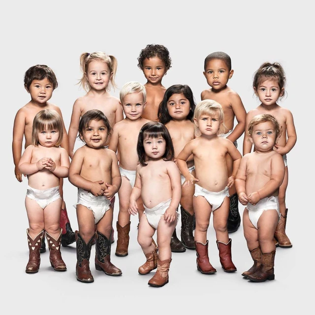 Group of toddlers wearing diapers and cowboy boots posing against a light grey backdrop in a studio setting.