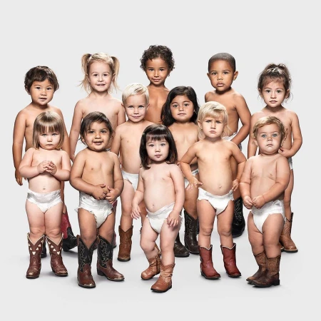 Group of toddlers wearing diapers and cowboy boots posing against a light grey backdrop in a studio setting.