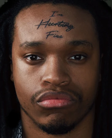 Close-up portrait of a Black adult male with dark dreadlocks, a serious facial expression, and the words 'I'm Hurting Fine' tattooed on his forehead.