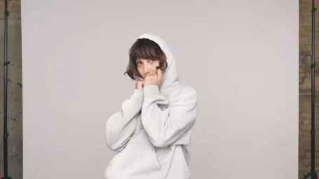 Woman in a white hooded sweatshirt pulling the hood up over her head in a studio portrait by Randal Ford.