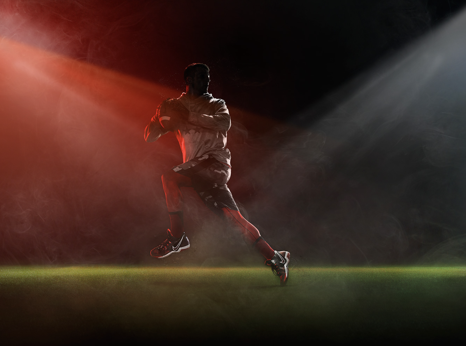 Silhouette of an adult male running with a football on a field in dramatic lighting and smoky atmosphere; sports, athlete, action.