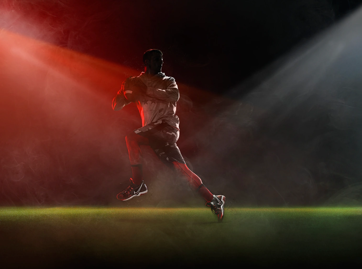 An American football player holding a football mid-air against dramatic red and white lighting with atmospheric haze.