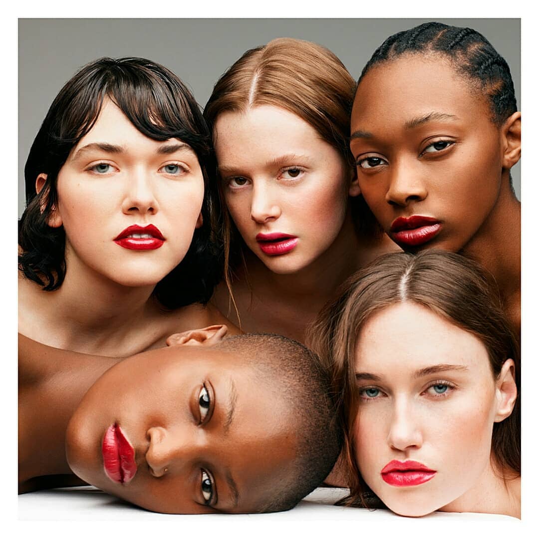 Close-up studio shot featuring five women of diverse ethnicities with red lipstick, showcasing beauty and fashion in a neutral setting.