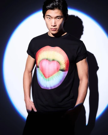 East Asian man wearing a black t-shirt with a rainbow lips graphic, posed against a circular blue spotlight backdrop.