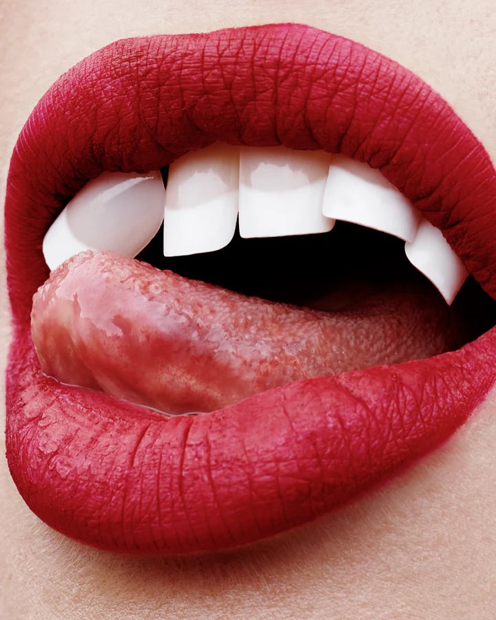 Extreme close-up of a woman's mouth with red lipstick and a tongue sticking out, showcasing dental and lip details.