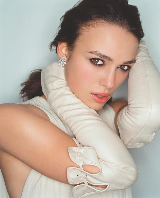 Close-up portrait of a woman with elegant makeup, wearing large floral earrings and long leather gloves in a studio setting.