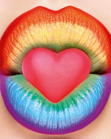 Close-up of rainbow-colored lips holding a pink heart-shaped candy, creating a vibrant and expressive beauty image.