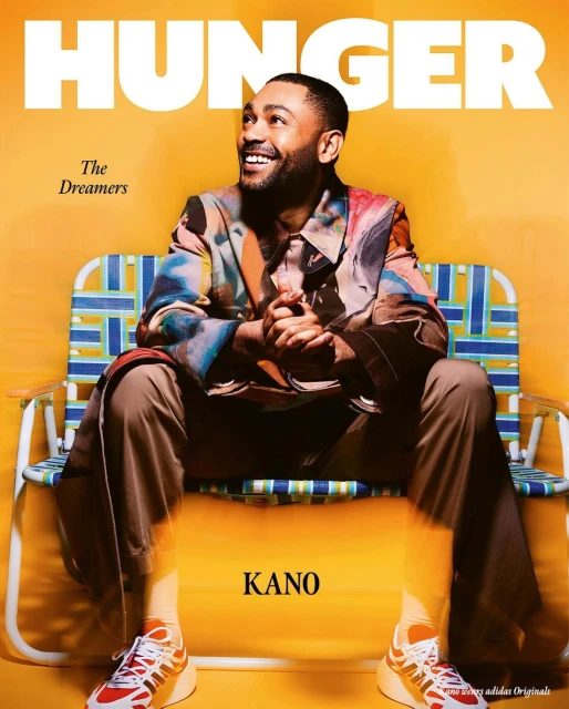 Magazine cover featuring a smiling man, Kano, seated on a blue and white lawn chair against a yellow backdrop, showcasing fashion and music.