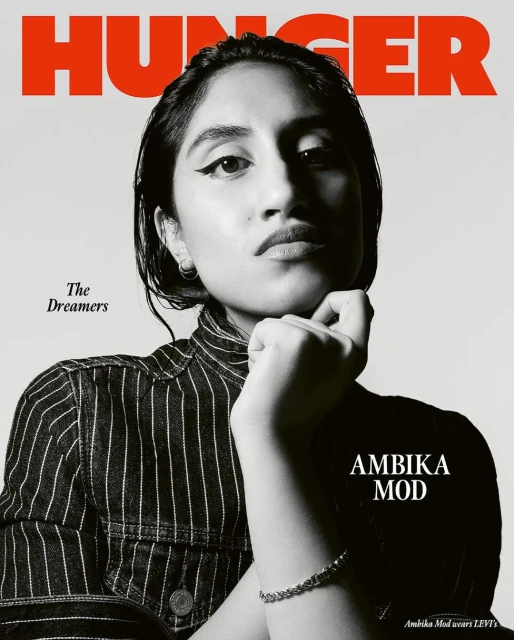 Close-up studio shot of Ambika Mod in a striped top, Hunger Magazine cover, neutral backdrop. The cover features the text 'HUNGER' and 'AMBICA MOD'.