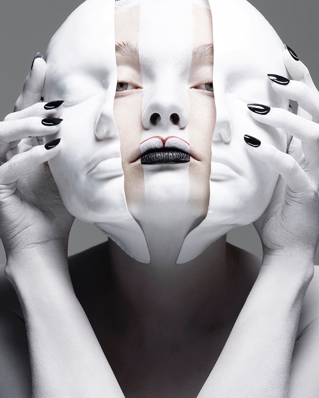 Striking close-up of a woman's face layered with white makeup and a deconstructed mask, set against a neutral gray background in a photo studio.