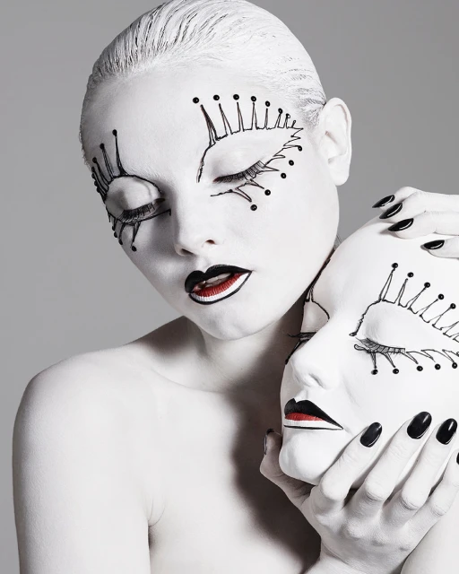Artistic portrait of a model with painted white skin, black lips, and theatrical makeup, holding a matching white mask.