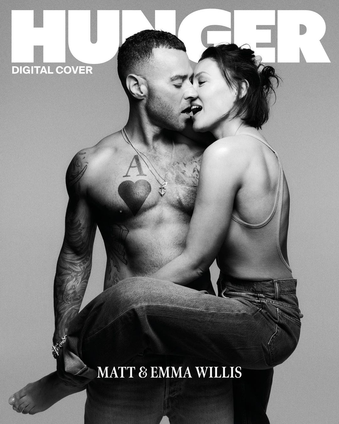 Black and white magazine cover featuring a shirtless man with tattoos holding a woman in his arms, both with mouths open.
