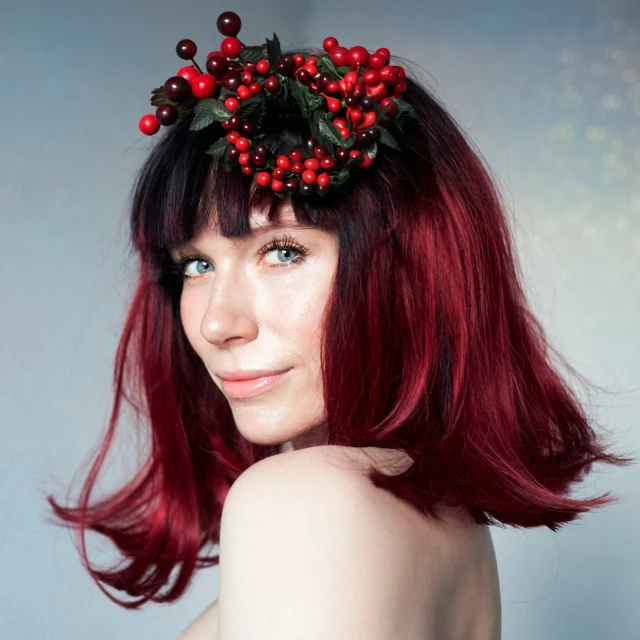 Portrait of a young adult woman with red-tinted hair, a berry headpiece, and a slight smile, captured in a close-up shot.