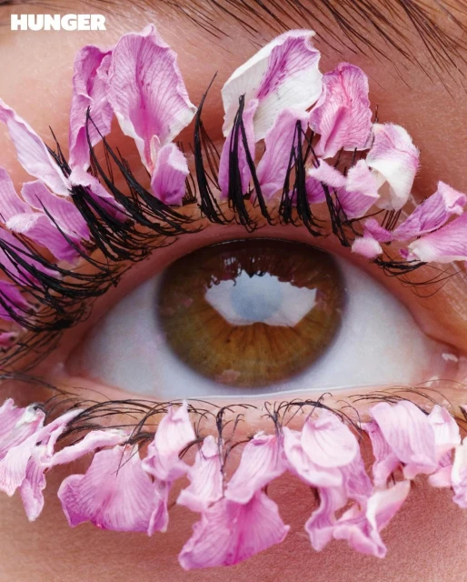 Close-up studio shot features an eye decorated with pink flower petals as eyelashes, creating a striking, floral-themed beauty statement.