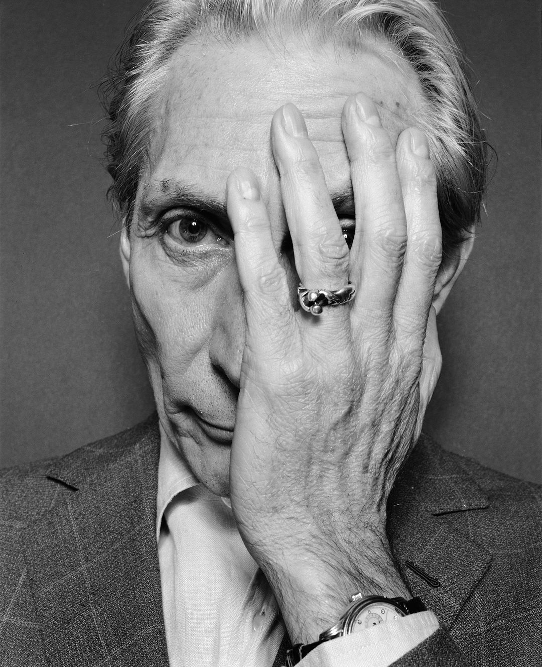 Black and white portrait of an adult male partially covering his face with his hand, wearing a suit and ring.