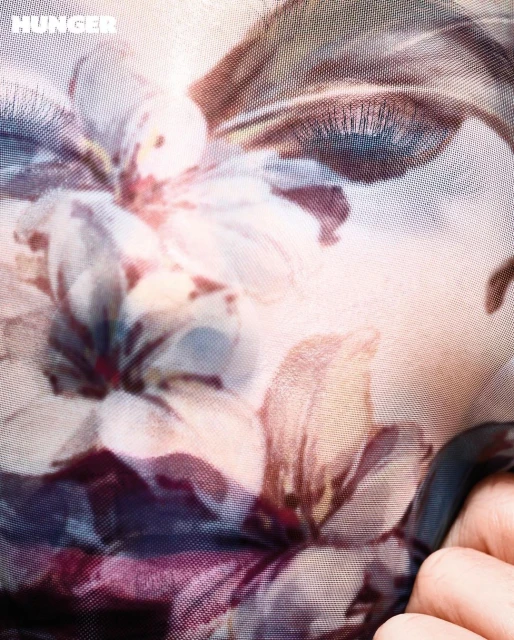 Close-up studio shot of a human face partially covered by a floral-patterned translucent fabric, highlighting an eye and fingers.