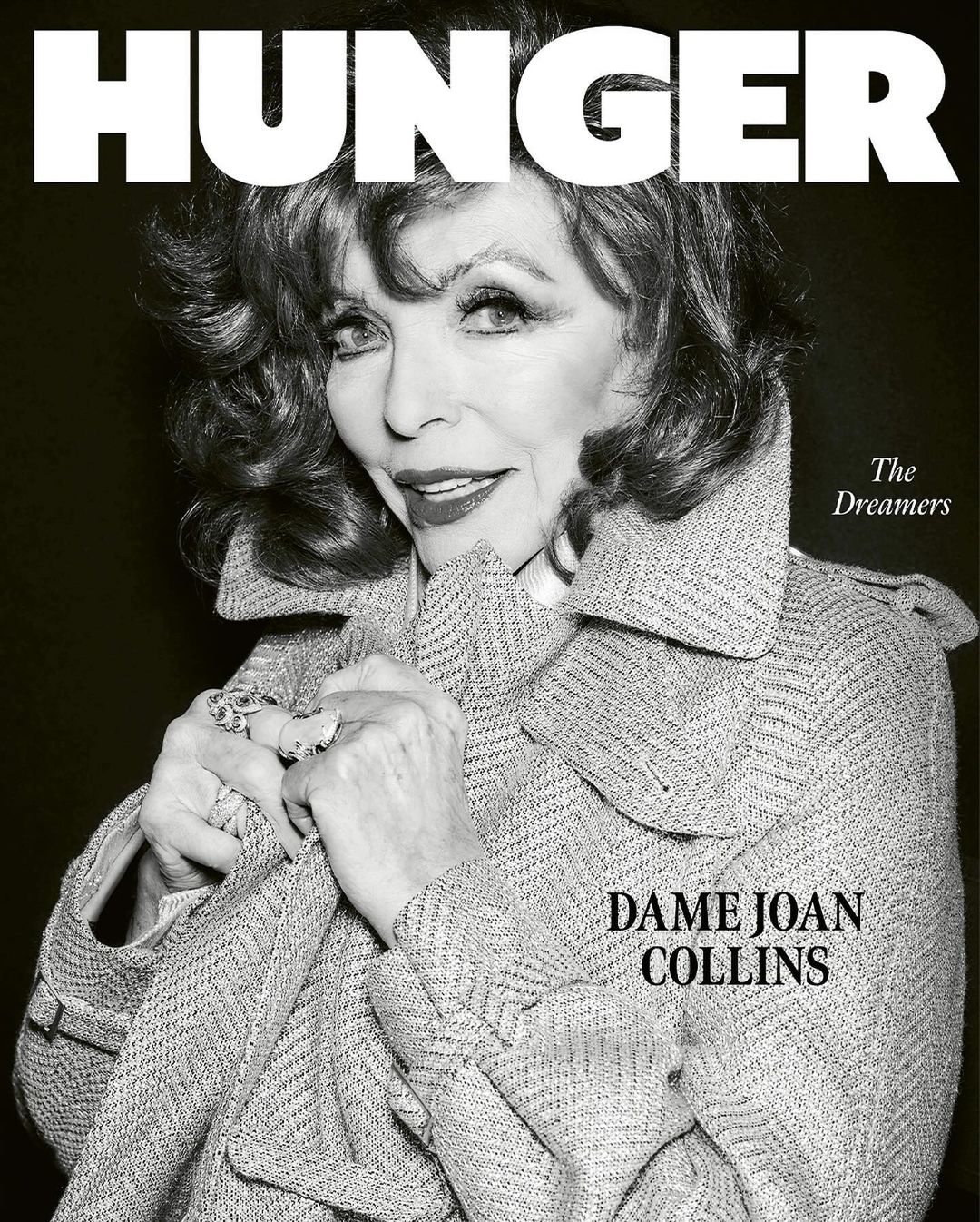 Black and white portrait of Dame Joan Collins on the cover of Hunger magazine, wearing a tweed coat and rings, against a dark backdrop.