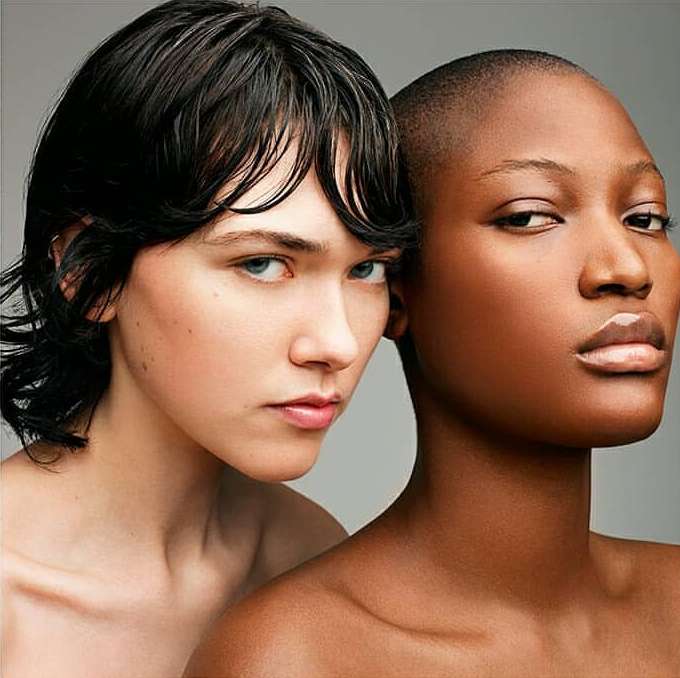 Close-up studio portrait of two diverse female models with shaved head and short hairstyle, showcasing skincare and beauty.