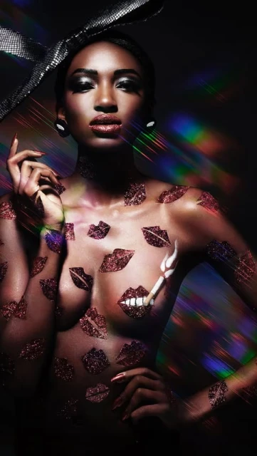 Striking portrait of a Black woman adorned with lip-shaped embellishments and a glittery bow, set against a dark backdrop with light effects.