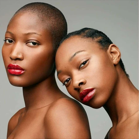 Portrait of two Black women with glossy red lipstick against a plain grey studio backdrop by Rankin