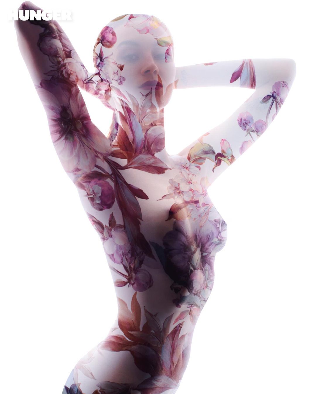 Artistic body art of a woman covered in floral designs in a full body suit, set against a bright white background.