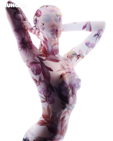 Artistic body art of a woman covered in floral designs in a full body suit, set against a bright white background.