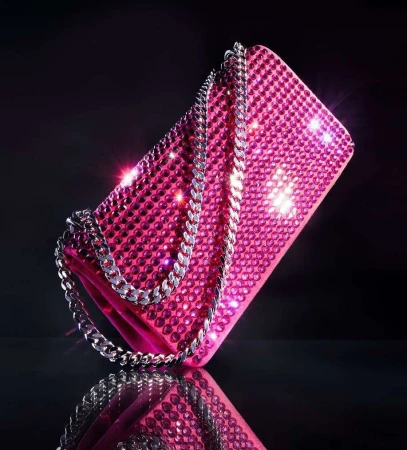 A sparkling pink rhinestone handbag with a silver chain strap against a dark background, photographed by Raymond Meier.