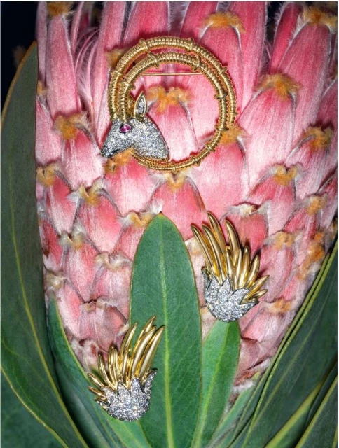 Gold and diamond horse brooch and earrings set on a light pink flower, showcasing jewelry design, nature, and luxury.