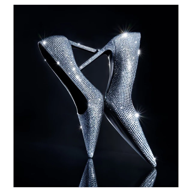 Elevated view of a pair of silver stiletto high heels adorned with rhinestones on a reflective black background, evoking glamour and luxury.