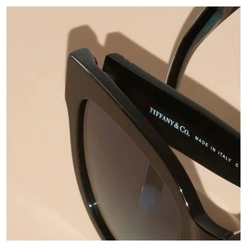 Close-up studio shot of black Tiffany & Co. sunglasses with gradient lenses and Tiffany & Co. branding on the side.