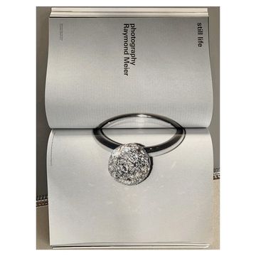 Close-up of a magazine page featuring a silver ring with a textured spherical diamond charm