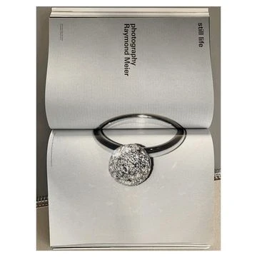 Close-up of a magazine page featuring a silver ring with a textured spherical diamond charm