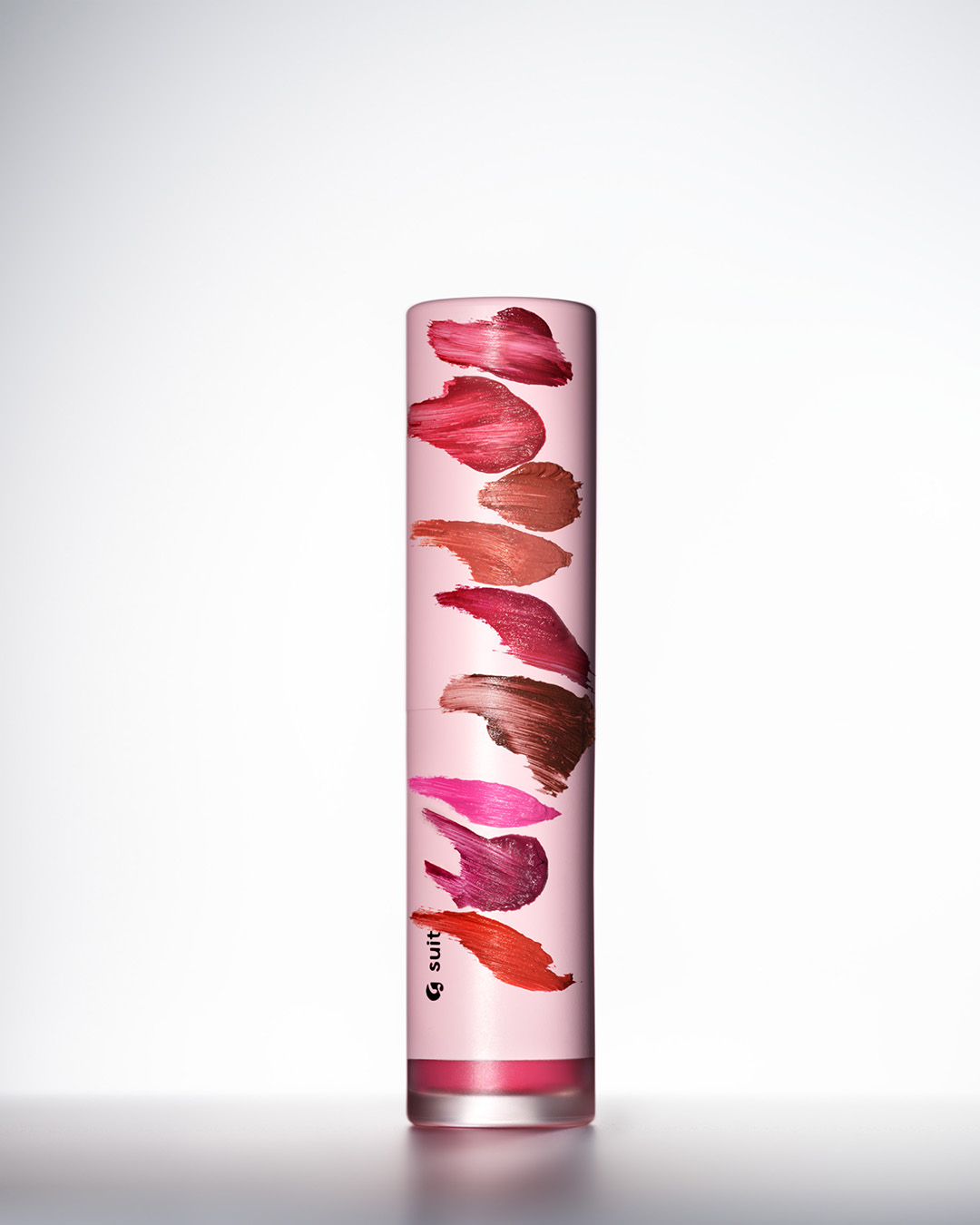 Close-up of lipstick tube with sample color swatches on the container, against a bright, neutral background in a studio setting.