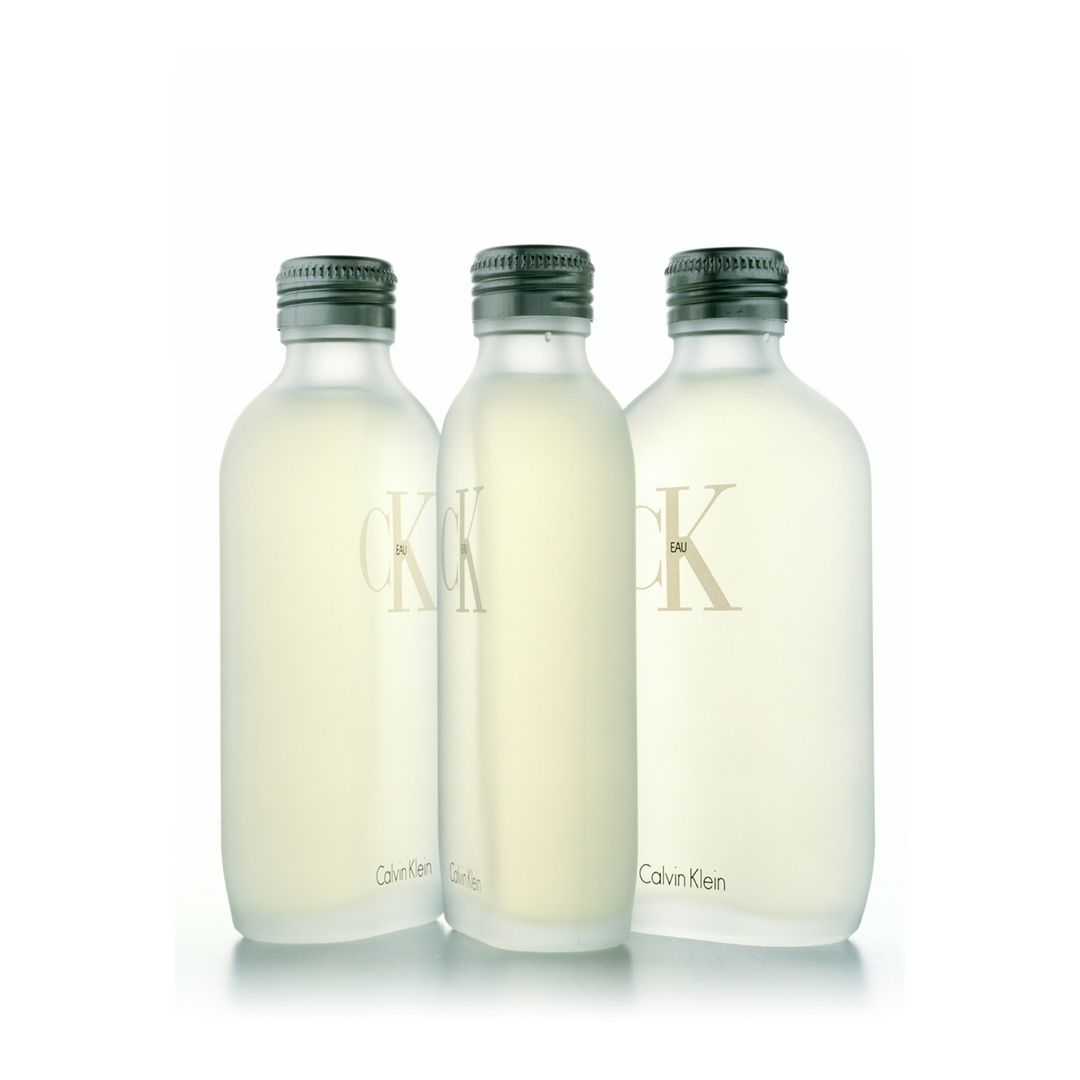 Three clear Calvin Klein CK One Eau de Toilette bottles stand in a row against a white background, displaying a minimalist aesthetic.