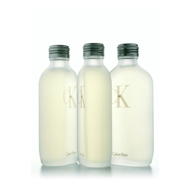 Three clear Calvin Klein CK One Eau de Toilette bottles stand in a row against a white background, displaying a minimalist aesthetic.