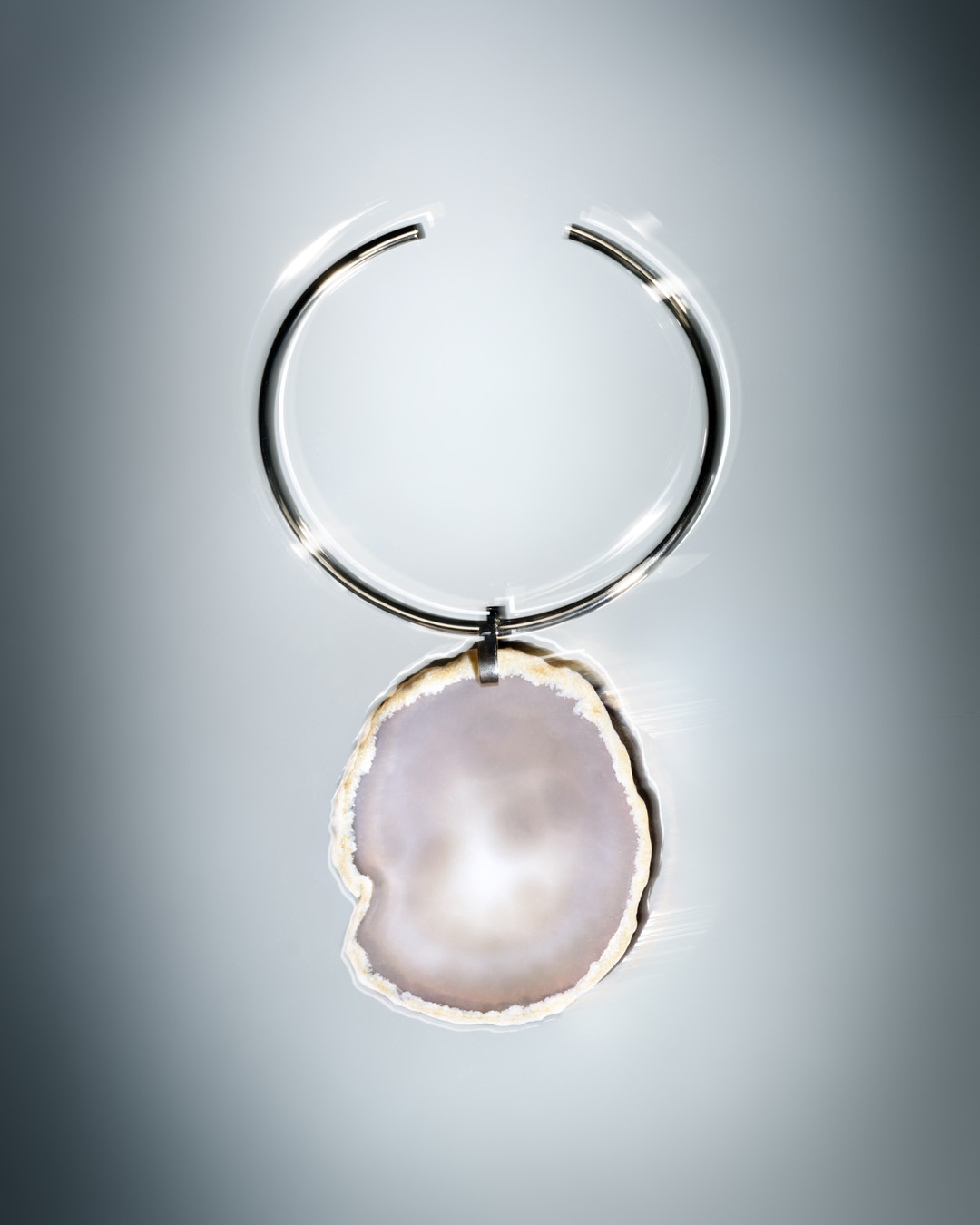 Pendant necklace with an open silver metal choker and a large organic white and cream colored pendant on a graduated gray background.