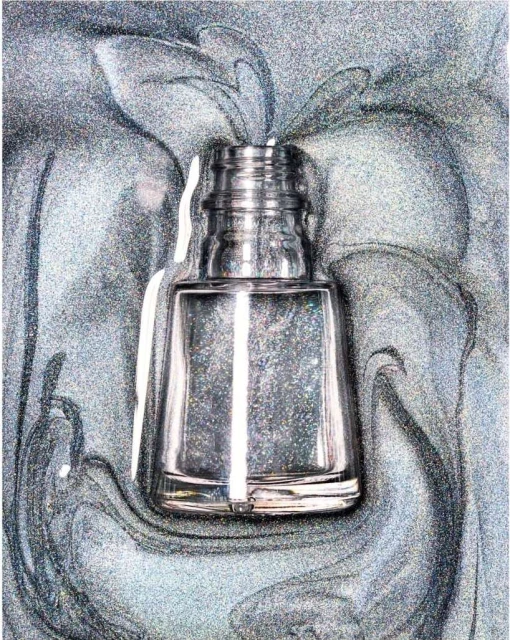 Overhead shot of a clear nail polish bottle against a swirling gray and silver background with light reflecting off the bottle.