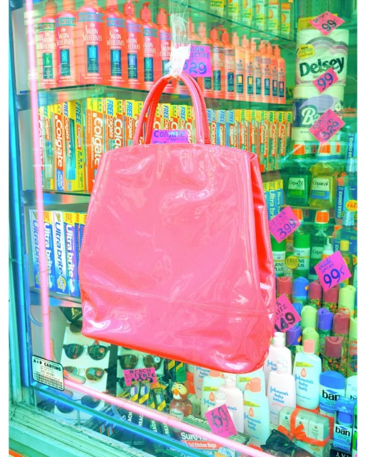 Eye-level shot of a pink handbag hanging against a glass display of toiletries and personal care items with pink price tags.