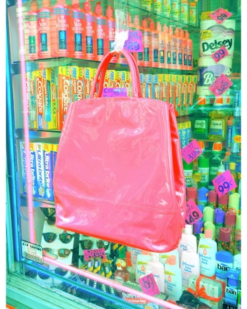 Eye-level shot of a pink handbag hanging against a glass display of toiletries and personal care items with pink price tags.