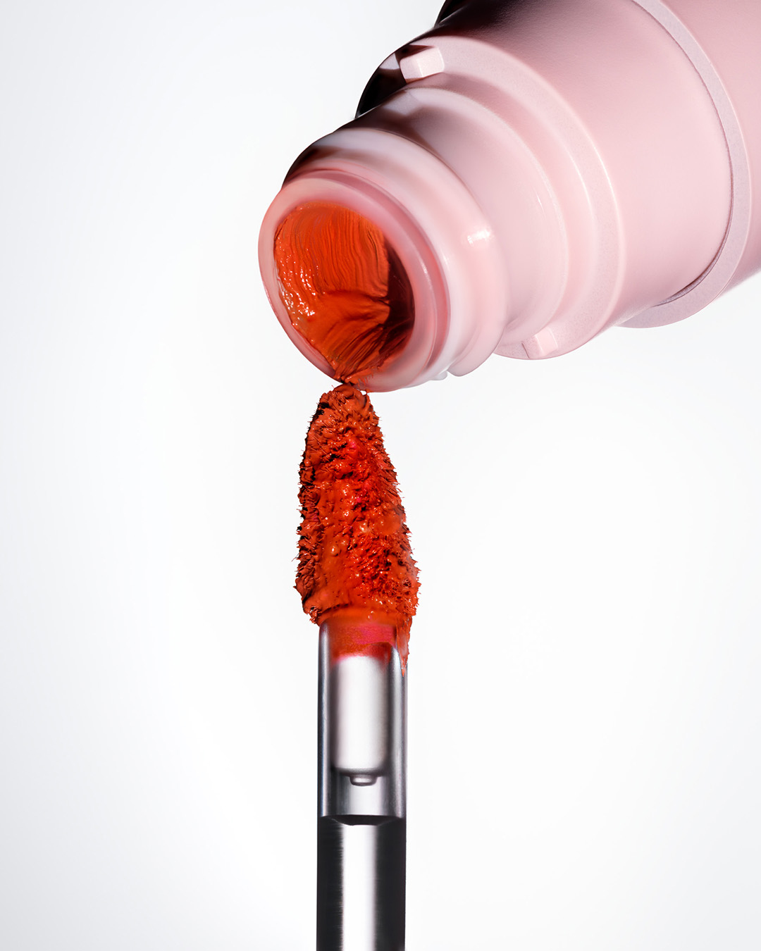 Macro shot of the pink container of orange lip gloss with an applicator on a white background, close up, beauty product shot.