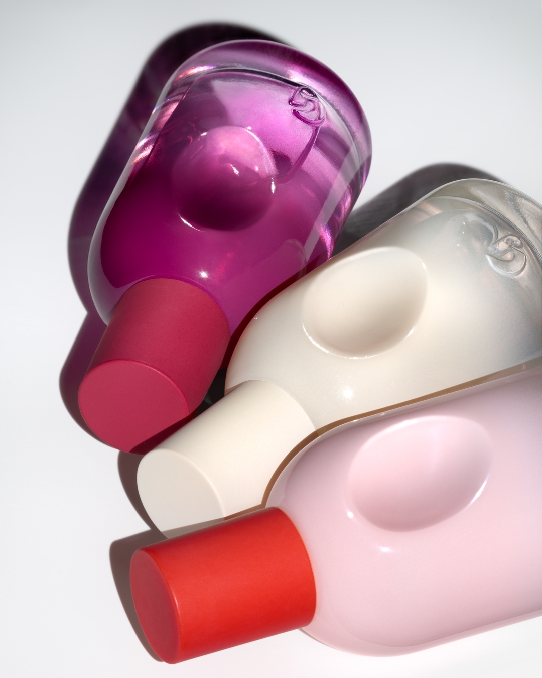 Three colorful plastic bottles with rounded shapes and cylindrical tops are neatly arranged on a bright white surface.