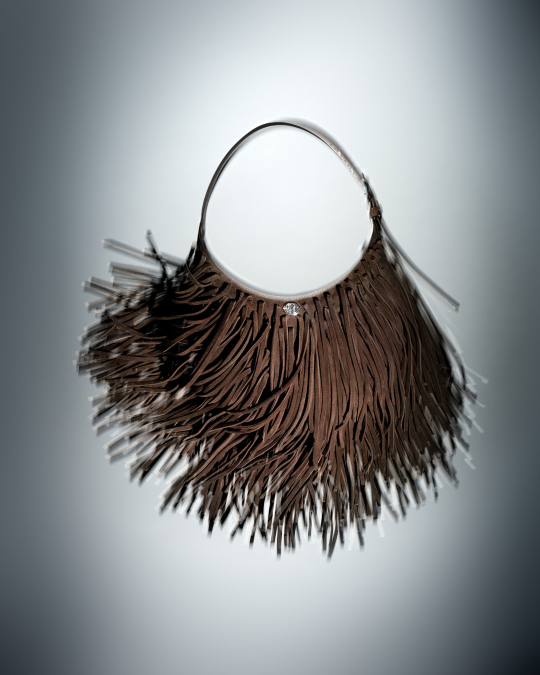 Fringed brown handbag on display in studio. The fashion bag is presented against a graduated grey backdrop with diffused lighting.