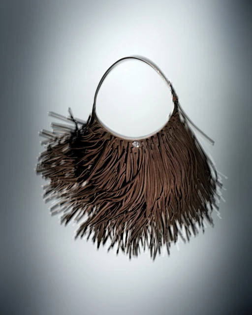 Fringed brown handbag on display in studio. The fashion bag is presented against a graduated grey backdrop with diffused lighting.