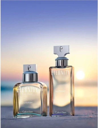 Two Calvin Klein Eternity Summer perfume bottles stand on a beach with a blurred sunset background, promoting a fresh, summery scent.